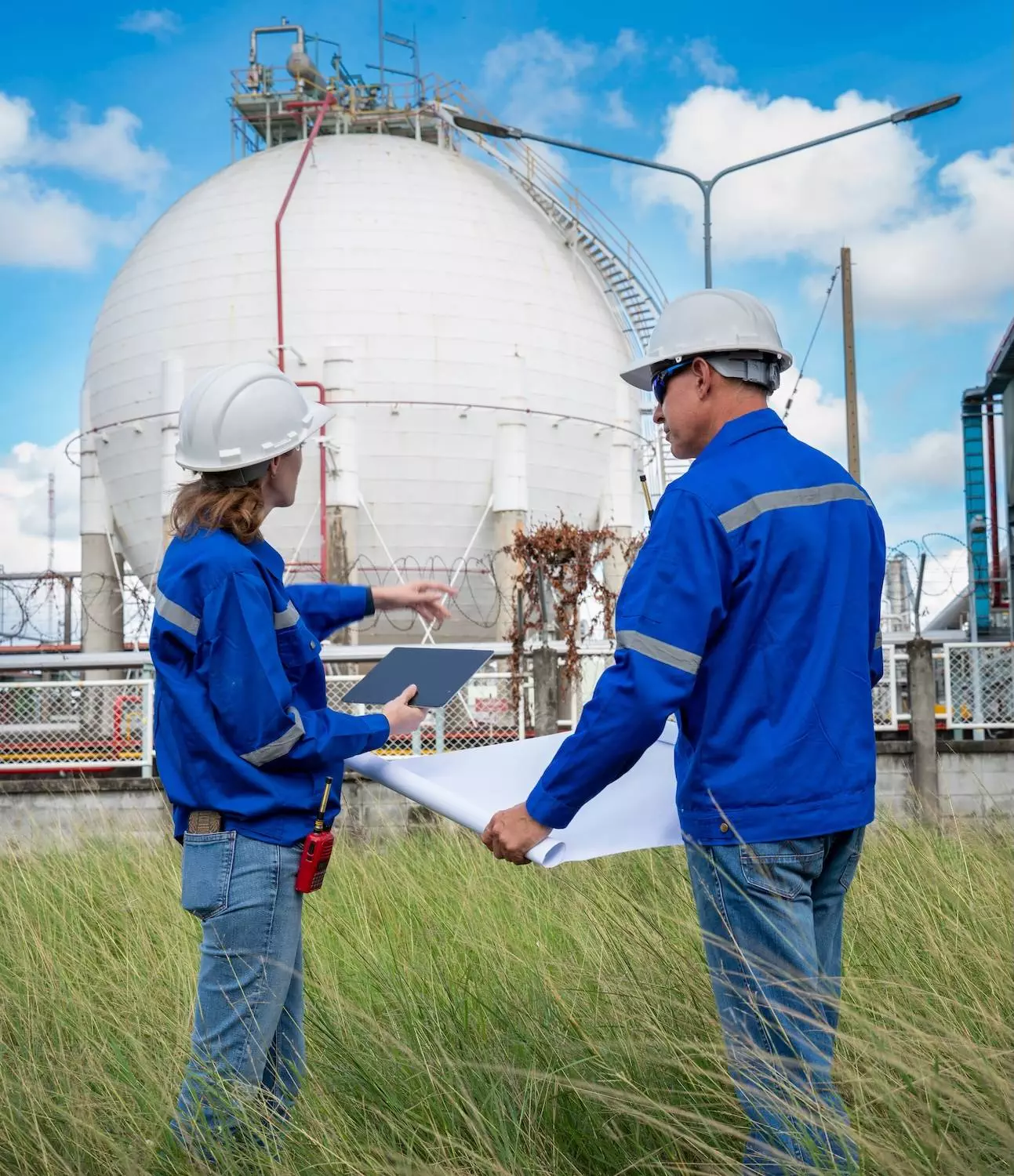 Two engineers reviewing technical plans in front of a gas processing facility